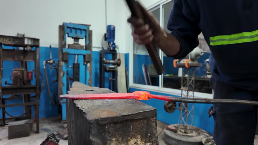Artisan blacksmith forging a custom knife blade with a hammer and anvil in a traditional workshop.