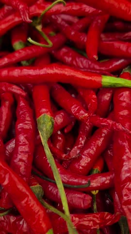 A vibrant pile of fresh red chili peppers with green stems fills the frame  overlaid with a white circular play button icon in the center.