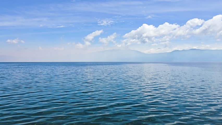 Calm Lake Water With Gentle Waves and Mountain View Under Blue Sky