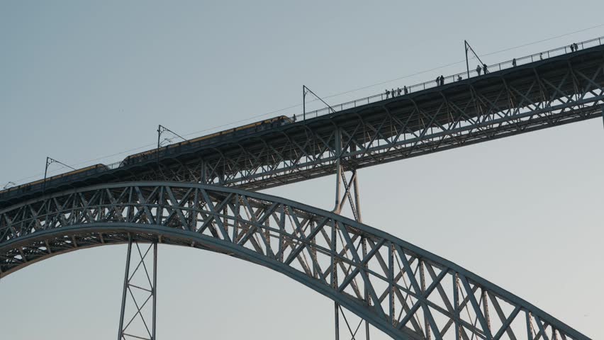Yellow metro train moving across the iconic iron bridge with pedestrians in Porto, Portugal.