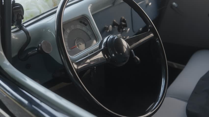 Close up of a classic vintage car interior focusing on the retro steering wheel and analog speedometer dashboard