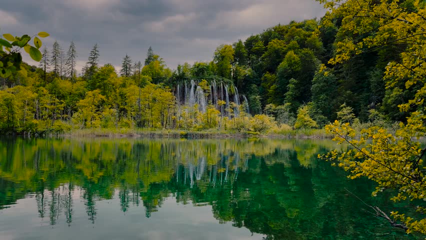 Waterfall cascading into emerald lake with perfect spring forest reflection, Plitvice Lakes, Croatia