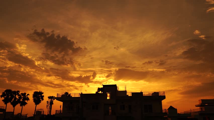Dramatic city skyline silhouette against a vibrant orange and dark sunset sky.