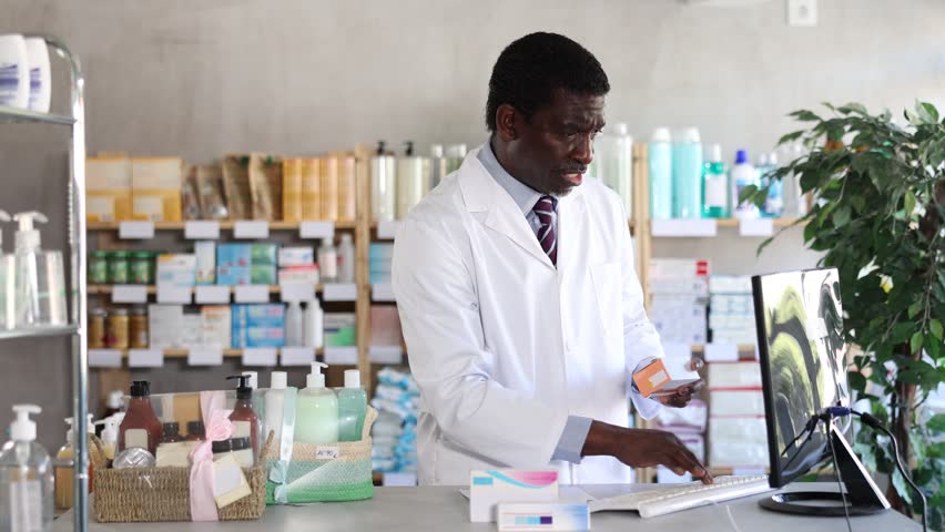 In sales area of pharmacy near computer, African man consultant offer and sells medication package. Healthcare worker advertises safe remedy for symptom relief