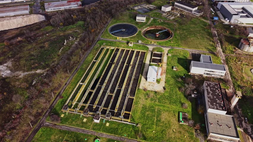 A water treatment plant shows large tanks and buildings surrounded by green land. The site operates daily to clean and treat water for the community. It is located near industrial areas.