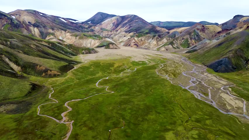 Colorful rhyolite mountains in Landmannalaugar Iceland highlands, cinematic drone shot, mineral rich volcanic landscape, green slopes and rivers at the bottom, lowland, plain with melting snow