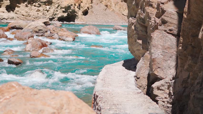 Slow motion shot of Tsarap river flowing with so many rocks in between obstructing the flow of river as seen during the trek to the Phugtal monastery in Zanskar, Ladakh, India. Nature background.