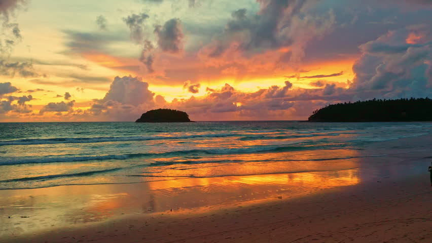 Aerial view of Island Glow at Kata Beach Phuket. The last rays of sunshine illuminate the clouds with vibrant colors, blending seamlessly with the turquoise waters, a perfect moment of peace and wonder.
