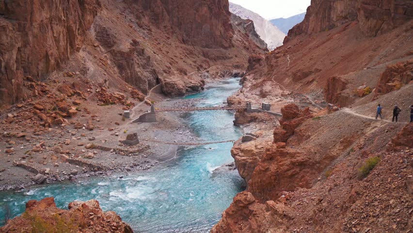 4K shot of beautiful mountain landscape with flowing blue river in Zanskar, Ladakh, India. Hikers hiking on narrow path on cliff. Turquoise blue Tsarap river in rocky Himalaya mountains. Travel and holidays concept.