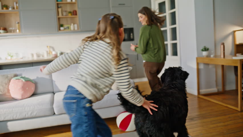 Family having fun with dog running together at home. Smiling girl adult woman spending time with playful pet enjoying canine love. Two owners playing with smart black animal fooling around apartment