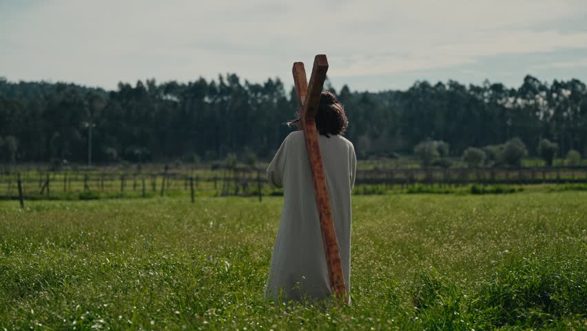 Rear view of Jesus Christ falling and disappearing into tall green meadow grass with cross