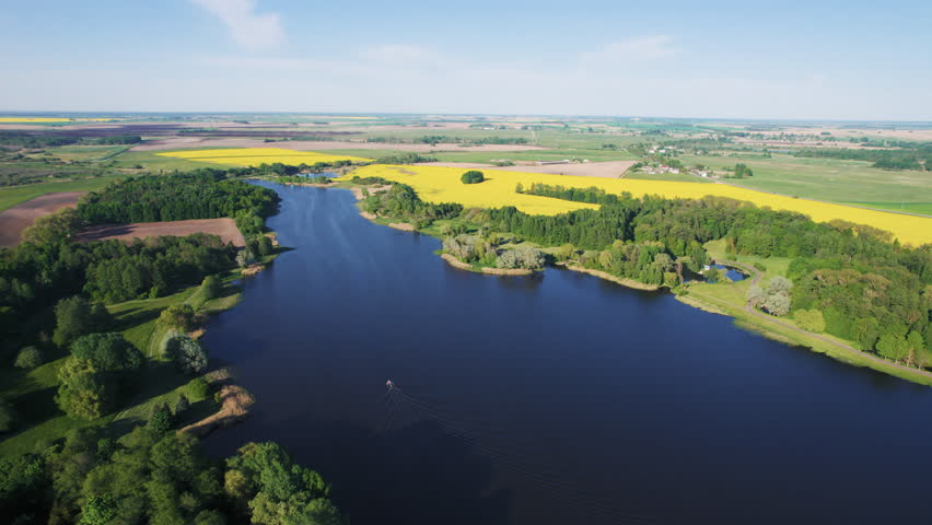Aerial view of a boat on a river next to blooming rapeseed fields