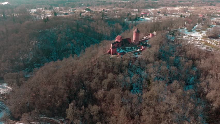Historic castle stands in the forest during winter time in a rural area with snow and trees surrounding the site and mountains in the distance
