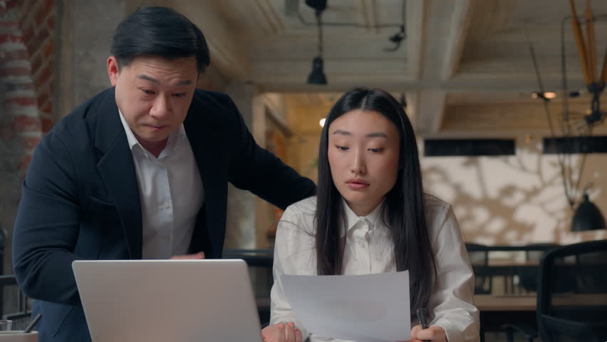 Two Asian business colleagues team problem documents sad intern angry boss in office Korean CEO boss businessman angry scolding unproductive incompetent Japanese Chinese businesswoman job mistake