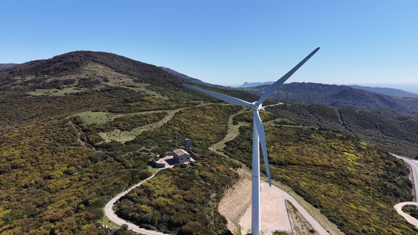 Aerial orbit around a wind turbine on a mountain ridge with a view of the Gibraltar strait in the Horizon.