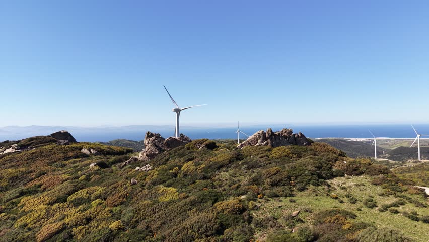 Wide aerial view of jagged rock formations on a mountain peak with wind turbines and the distant Strait of Gibraltar, with Africa in the Horizon.