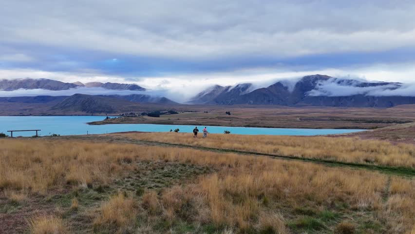 Tourists run through mountain plateau grass to Lake Tekapo, New Zealand