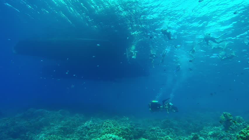 Group of snorkelers swims in the coral garden next to diving boats, scuba divers swimming underneath them, Slow motion of boat over coral reef, tourists and scuba floats nearby, Red Sea, Egypt 