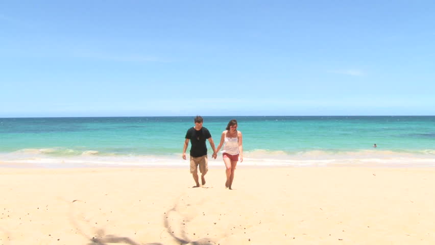 Happy woman and man couple walk together, holding hands on sandy beach.