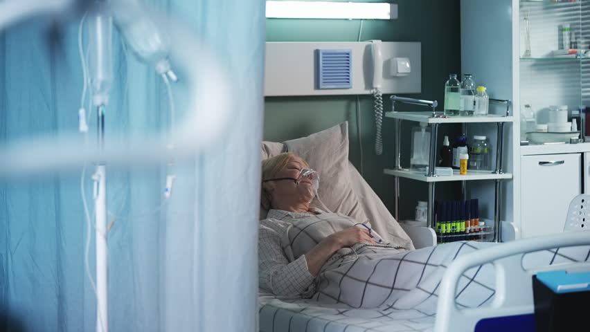 Ill senior woman in oxygen mask lying in ICU bed, receiving intensive care
