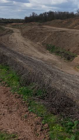 Panshanger quarry landscape with a low, slow right vertical pan over excavated earthworks, dirt access road, and grassy banks under bright spring sky with scattered clouds.