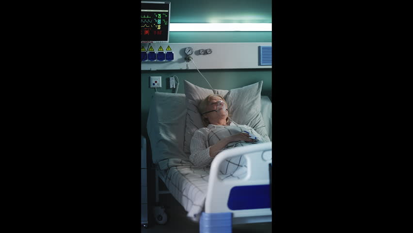 Senior woman wearing oxygen mask lying in ICU bed, intensive medical care