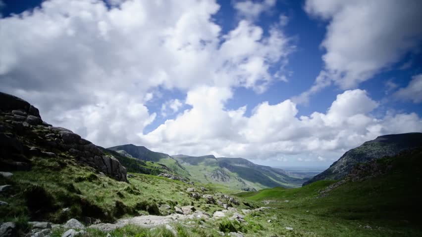 Lake District wide mountain valley with rocky foreground rolling green hills and dramatic clouds creating scenic natural landscape in bright outdoor setting