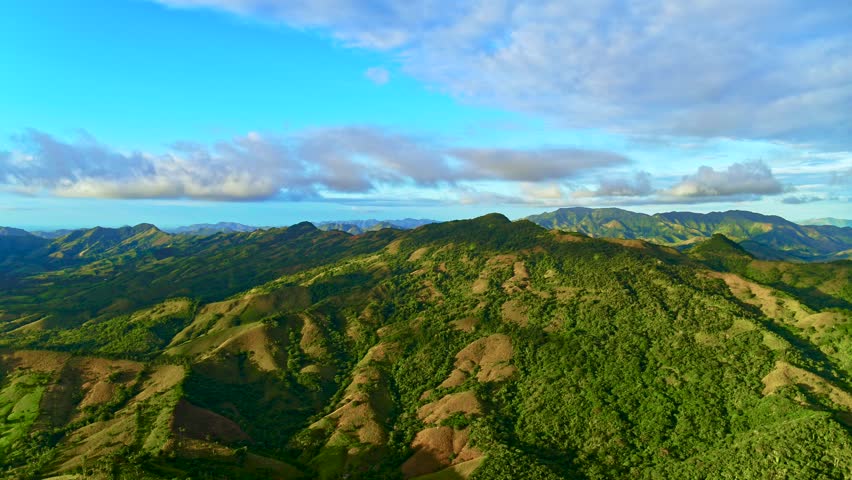 Dominican Republic mountain peaks in the morning light under a cloudy sky. Summer in the Dominican mountains. Picturesque panoramic view of an idyllic landscape of rolling hills with tropical forests on a beautiful sunny day.
