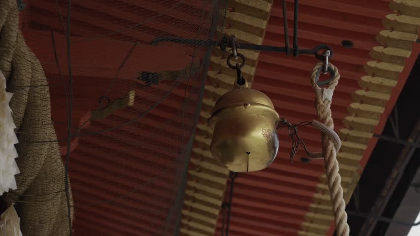 Large brass bell suspended by chain and thick rope beneath red painted wooden shrine ceiling, Kyoto Japan