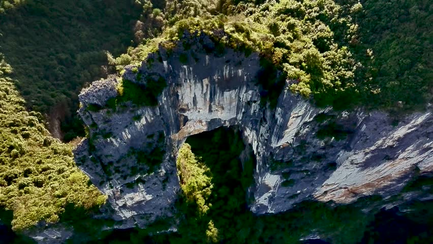 A majestic natural stone arch formation surrounded by lush green foliage in a deep forest setting
