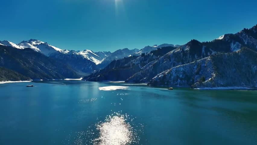A serene view of a crystal clear blue alpine lake surrounded by majestic snow-capped mountains