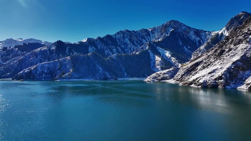 A serene view of a deep blue lake nestled against tall snow capped mountains under clear sky