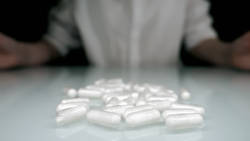 Female hands gathering white capsules on table concept of medication intake dosage healthcare treatment and pharmaceutical use.