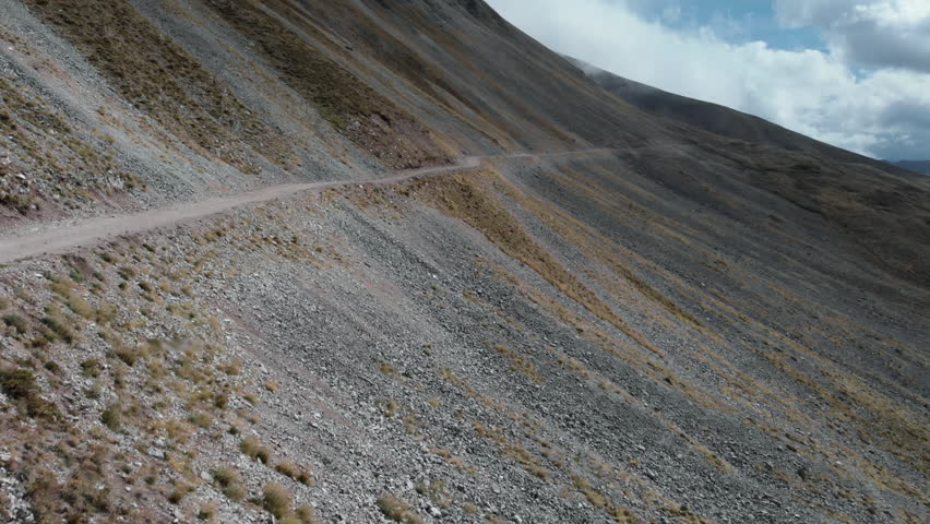 A winding mountain road cuts through a steep, rocky slope under expansive blue skies. Ideal for travel and adventure themes.