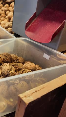 Vertical close-up of an industrial walnut cracking machine in a nut shop, cracked walnuts falling into a container, mobile-friendly social media format for food industry and healthy snacks.
