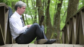 A young handsome businessman sitting on a bridge and using laptop
