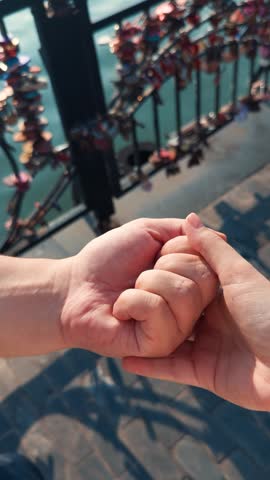 Hand offering a heart shaped key symbolizing commitment and trust in a loving relationship, with blurry love locks on a bridge fence over water in the background