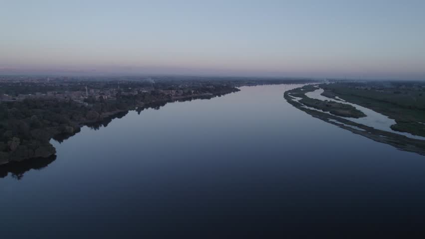 Aerial drone shot of the Nile River in Upper Egypt with natural landscape, green fields and traditional environment. Scenic view of the river and rural surroundings.
