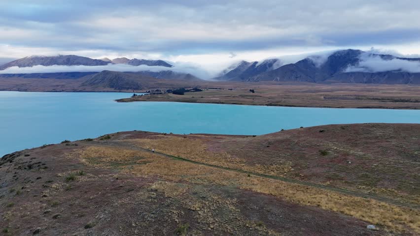 Aerial pulls out form pale blue mountain Lake Tekapo in New Zealand