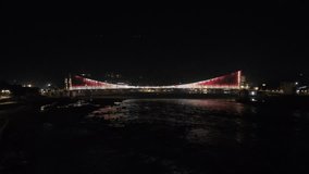 A cinematic night shot of the Janaki Setu,Ram Setu,Laxman Setu suspension bridge in Rishikesh, Uttarakhand. The footage captures the vibrant, synchronized LED light show reflecting on the Ganges River, showing the modern architecture of the three-lane bridge against the dark Himalayan backdrop. - Powered by Shutterstock - Get 15% off with code: PIKWIZARD15