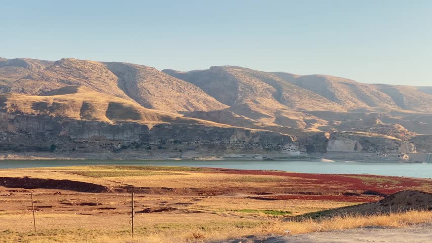 Iconic sun-drenched arid mountain rises above Hasankeyf Dam tranquil blue lake reservoir in Turkey