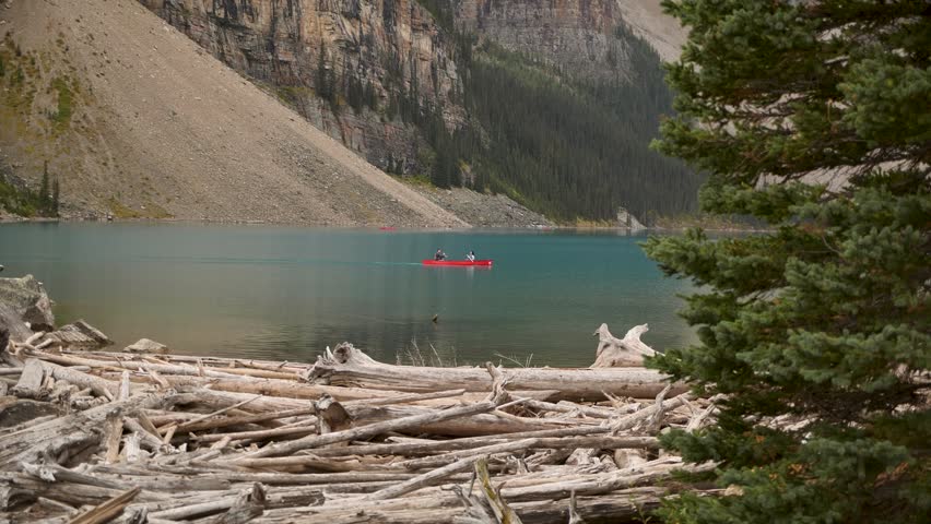 Majestic scenery of Moraine Lake with two people canoeing on the glacial turquoise water against the Valley of the Ten Peaks, Banff National Park, Canada. Road trip in Canada. Rocky mountains. 4k.