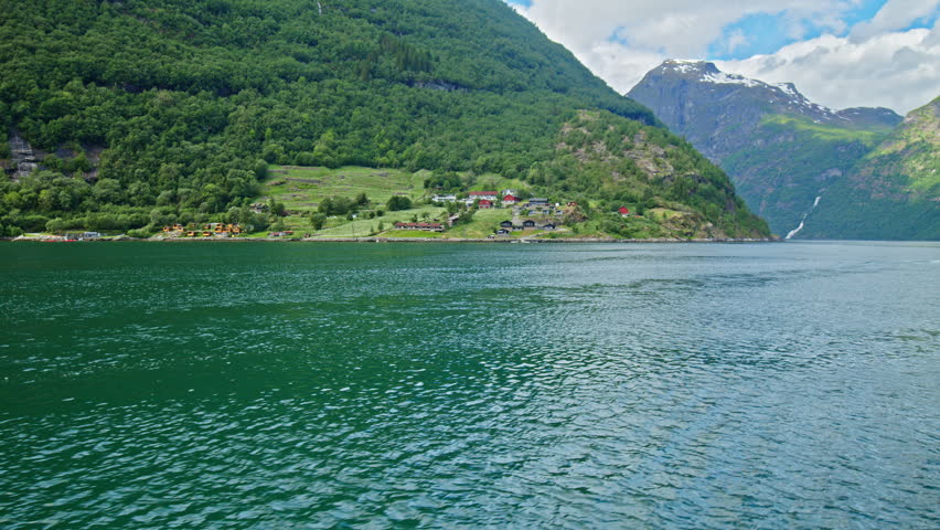 Fjord shoreline with small settlements and lush hills along Geirangerfjord. Peaceful rural landscape on the way to Skagefla in Norway.