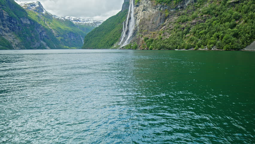 Fjord with waterfall and towering cliffs along Geiranger route in Geirangerfjord. UNESCO-listed landscape in Norway.