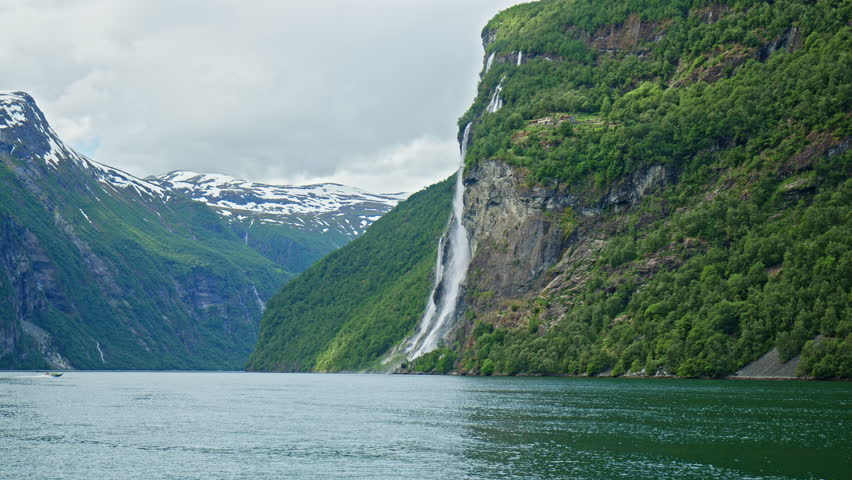 Tall waterfall flowing down steep cliffs into fjord in Geirangerfjord. Famous fjord scenery in Norway.