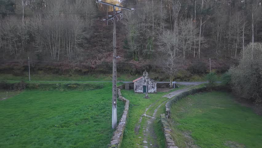 Old stone chapel standing in a green field with a forest background