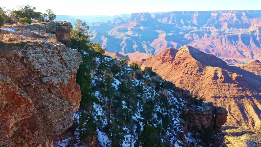 Wide panoramic view of Grand Canyon cliffs and layered landscape under warm sunset light from above