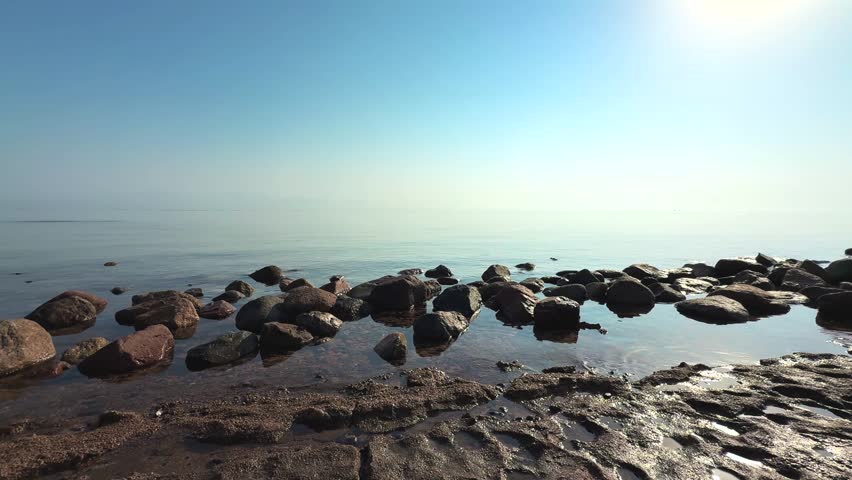 Morning Light Over Still Sea with Scattered Coastal Rocks. Beautiful tranquillity wide landscape of nature