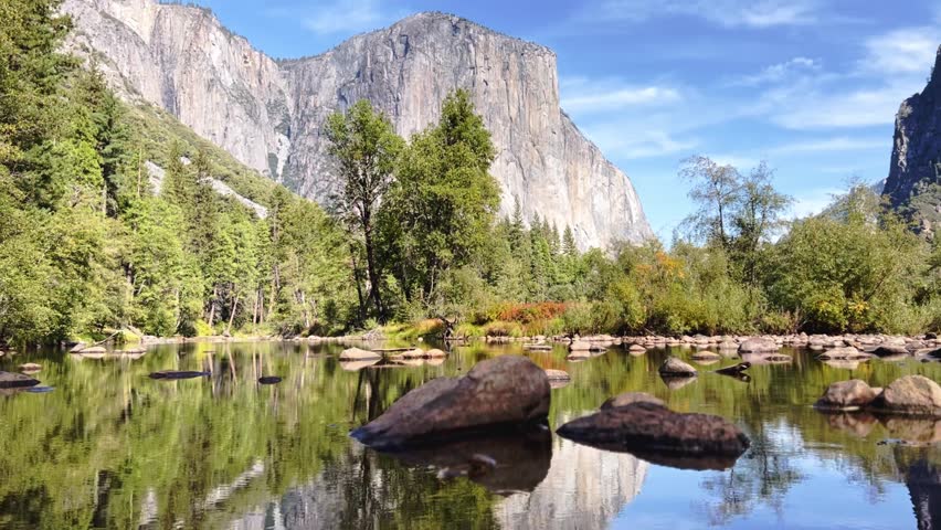 El Capitan reflects clearly in still water with surrounding forest and rocks in Yosemite Valley.
