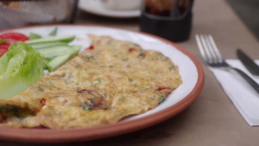 Slow motion video shows appetizing homemade omelette with tomatoes, cucumbers, and lettuce, healthy food for brunch.